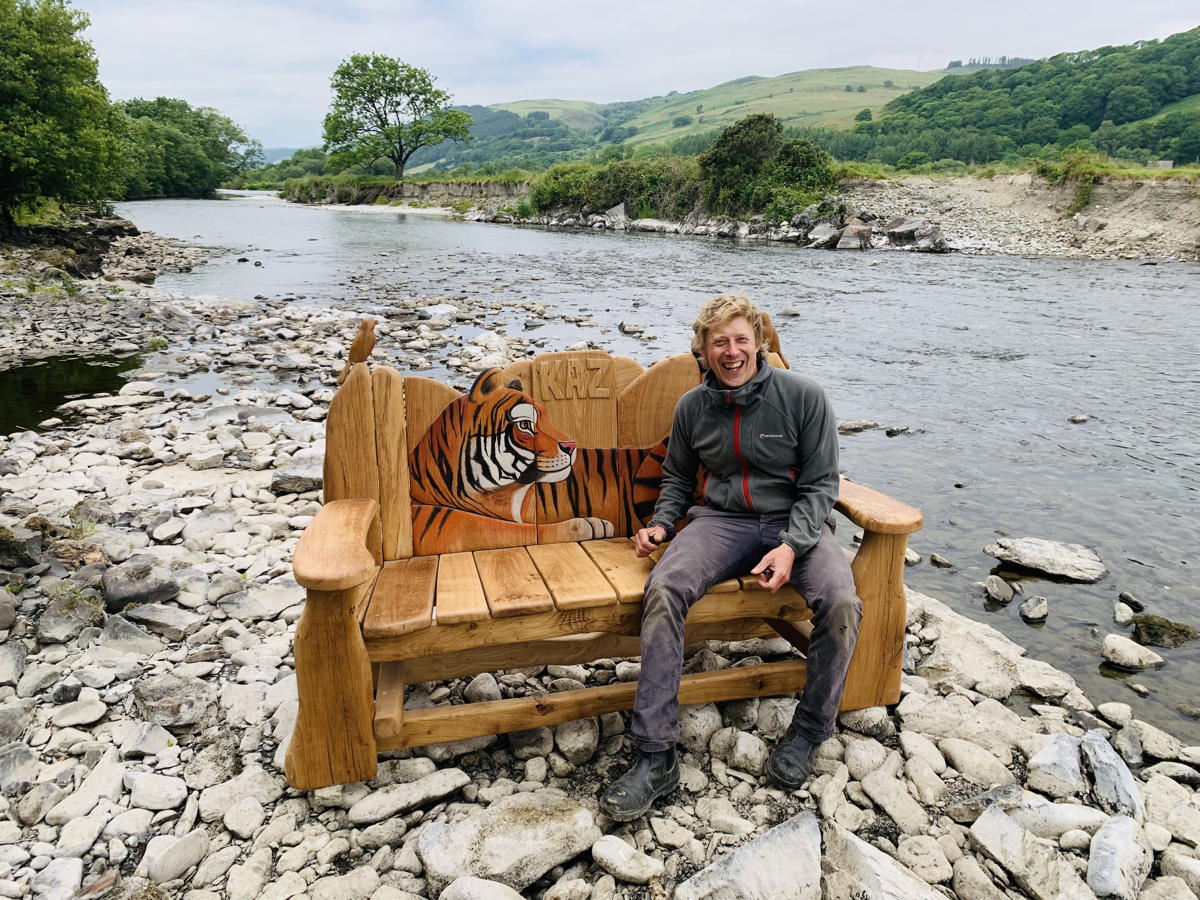 Person sitting on a tiger-themed wooden bench by a river