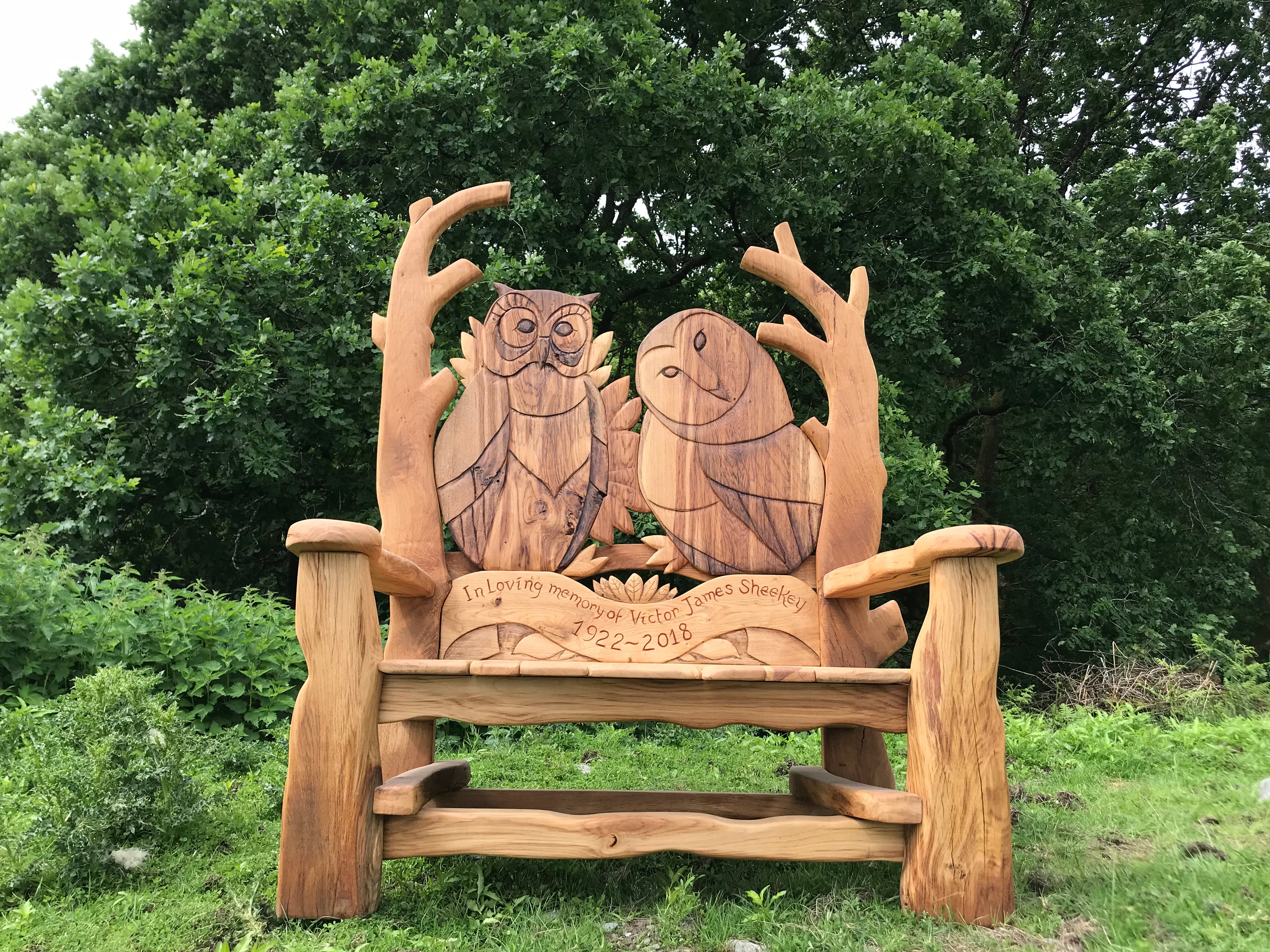 Memorial wooden bench with owl carvings in nature.