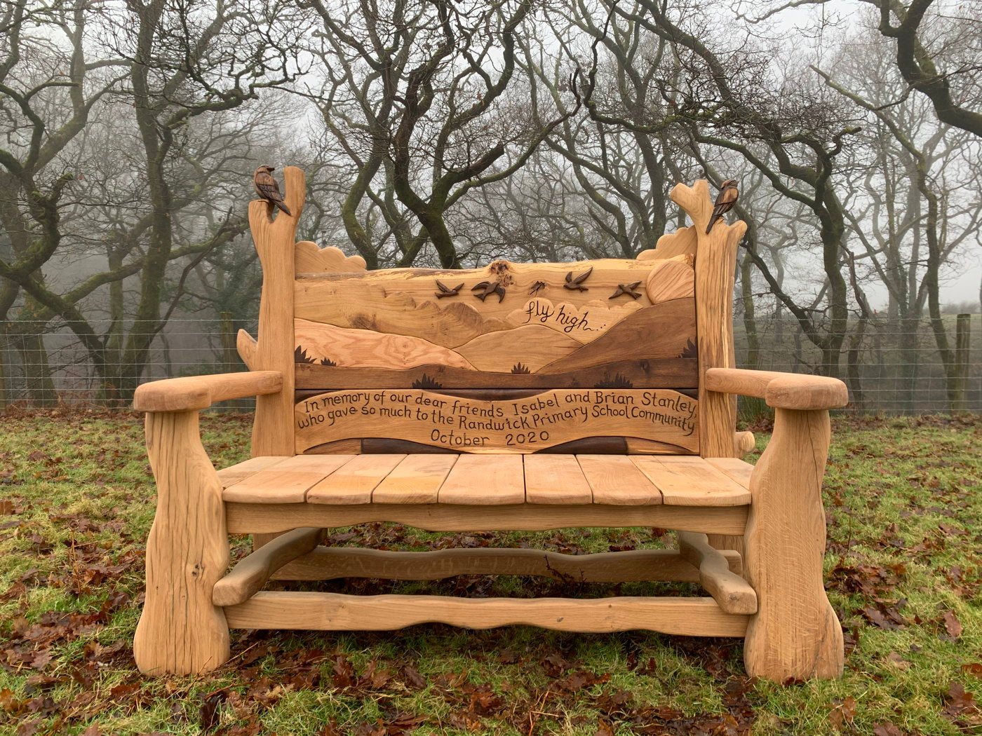 Memorial bench with landscape carving and dedication.